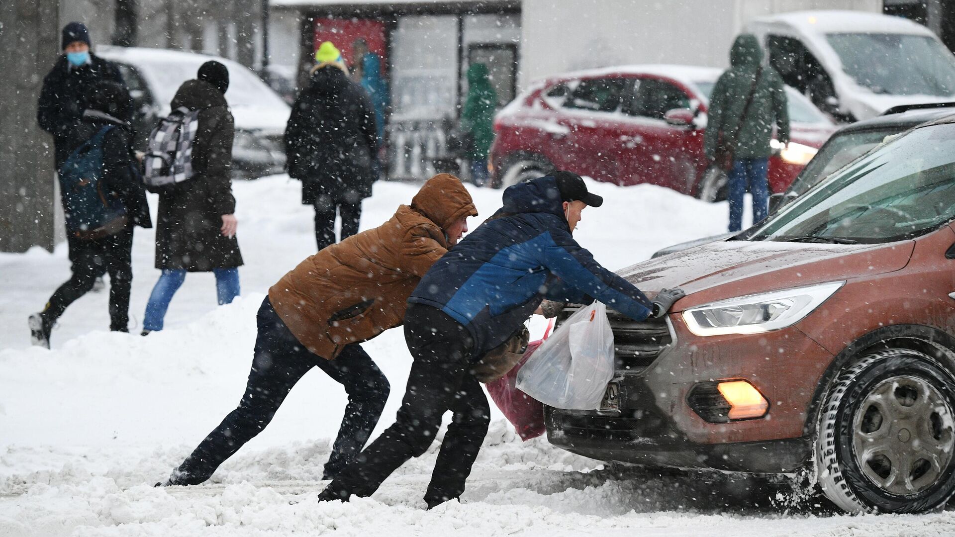 Мужчины толкают машину, застрявшую на дороге во время снегопада - РИА Новости, 1920, 21.01.2021