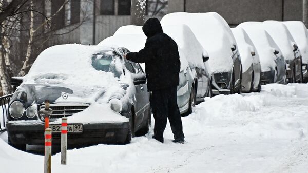 Мужчина очищает автомобиль от снега в Москве