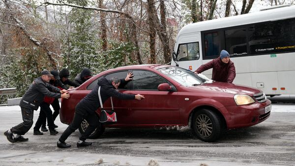 Мужчины толкают машину на одной из улиц в Сочи