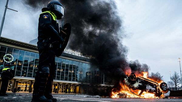 Автомобиль, подожженный в ходе антикоронавирусного митинга, горит напротив вокзала в городе Эйндховен, Нидерланды