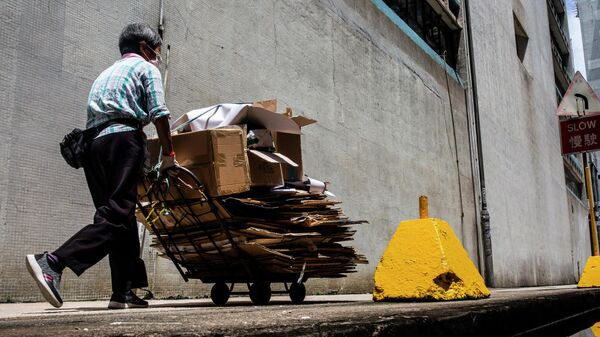 Женщина толкает корзину с картоном в Гонконге 