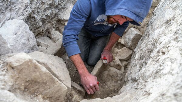 Участник экспедиции зачищает камин на дне могильной ямы во время исследования грунтового могильника Киль-Дере близ Севастополя