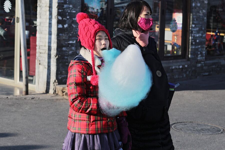 Женщина в защитной маске и девочка с сахарной ватой на улице Пекина