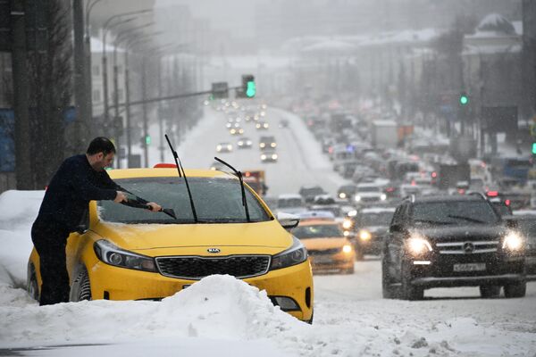 Мужчина чистит от снега и наледи автомобиль во время снегопада в Москве