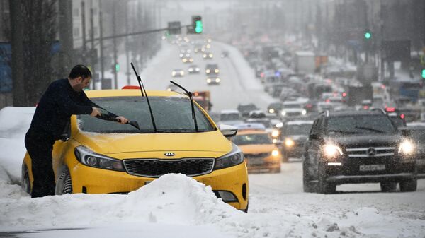 Мужчина чистит от снега и наледи автомобиль во время снегопада в Москве