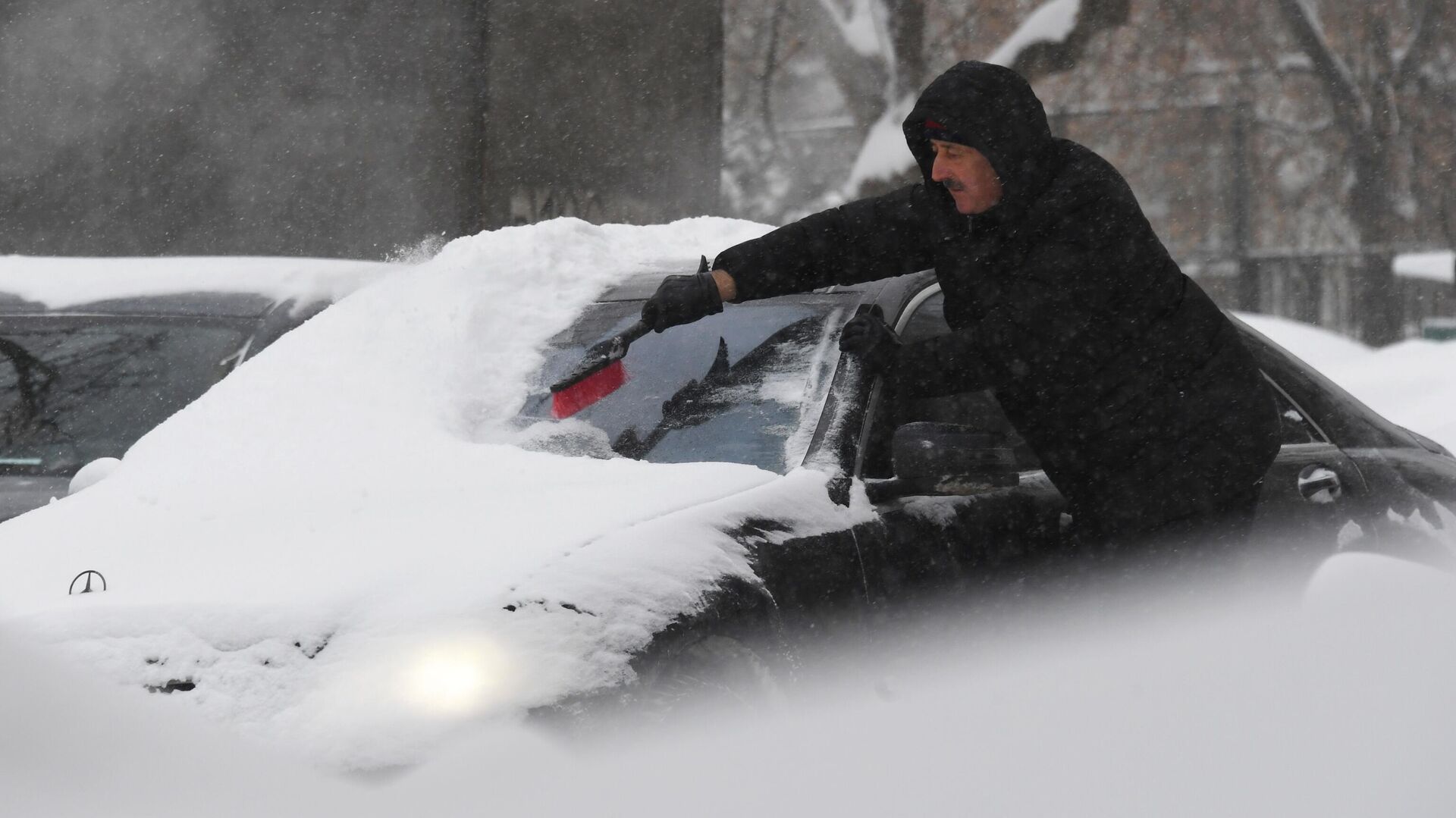 Житель Москвы чистит машину от снега во время снегопада - РИА Новости, 1920, 26.11.2021