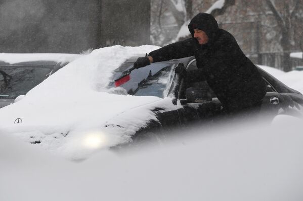 Житель Москвы чистит машину от снега во время снегопада