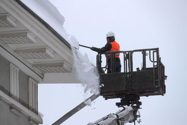 Работник коммунальной службы убирает снег с крыши здания музея Москвы на Зубовском бульваре в Москве
