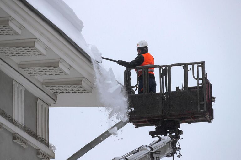 Работник коммунальной службы убирает снег с крыши здания музея Москвы на Зубовском бульваре в Москве