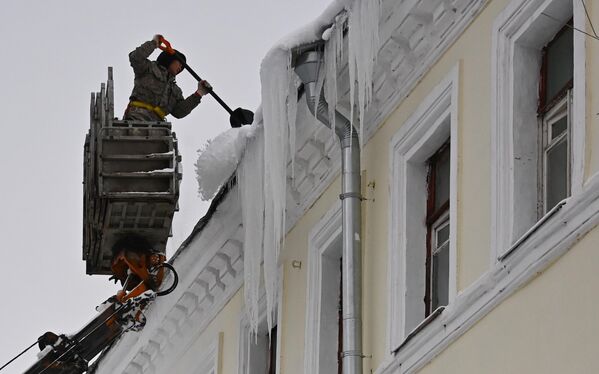 Сотрудник коммунальной службы счищает снег с крыши дома в Посланниковом переулке в Москве