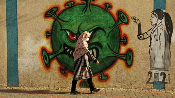 Женщина проходит мимо граффити, посвященного коронавиурсу, в Газе