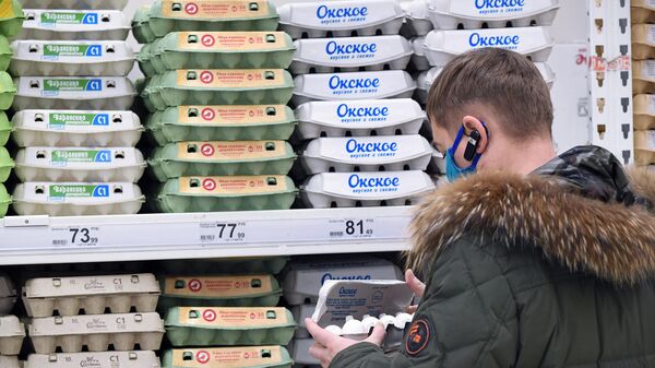 Покупатель выбирает упаковку с яйцами в гипермаркете Ашан в Москве