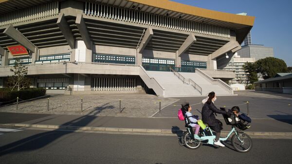 Женщина с детьми проезжает мимо арены Ниппон Будокан в Токио