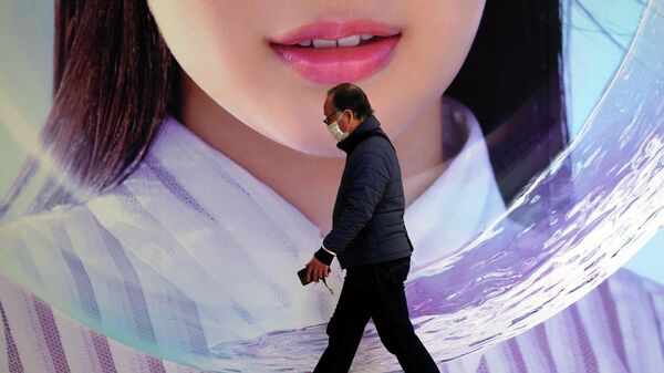 Мужчина в защитной маске проходит мимо рекламного щита в Токио