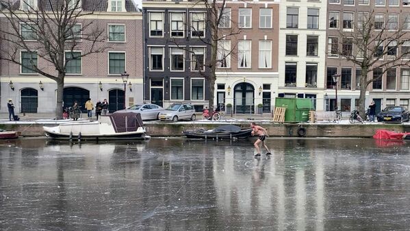Мужчина катается на коньках по каналу Кайзерсграхт в Амстердаме, Нидерланды