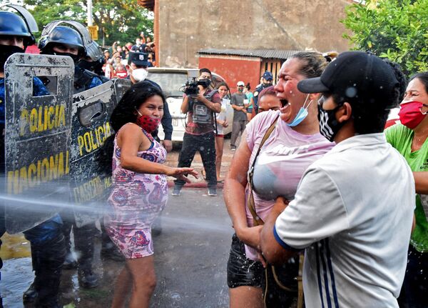 Полиция опрыскивает водой родственников заключенных во время акции протеста у тюрьмы Такумбу в Асунсьоне, Парагвай