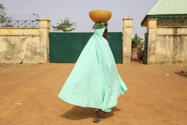 Девушка с чашей молока у ворот школы в Нигерии, где были похищены более 300 учениц