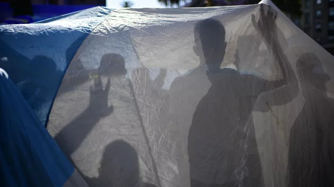 Fans are seen behind an Argentinian flag as they wait outside the Casa Rosada government house to pay their tribute to Argentinian late football legend Diego Armando Maradona in Buenos Aires, on November 26, 2020. - Argentine football legend Diego Maradona will be buried Thursday on the outskirts of Buenos Aires, a spokesman said. Maradona, who died of a heart attack Wednesday at the age of 60, will be laid to rest in the Jardin de Paz cemetery, where his parents were also buried, Sebastian Sanchi told AFP. (Photo by RONALDO SCHEMIDT / AFP)