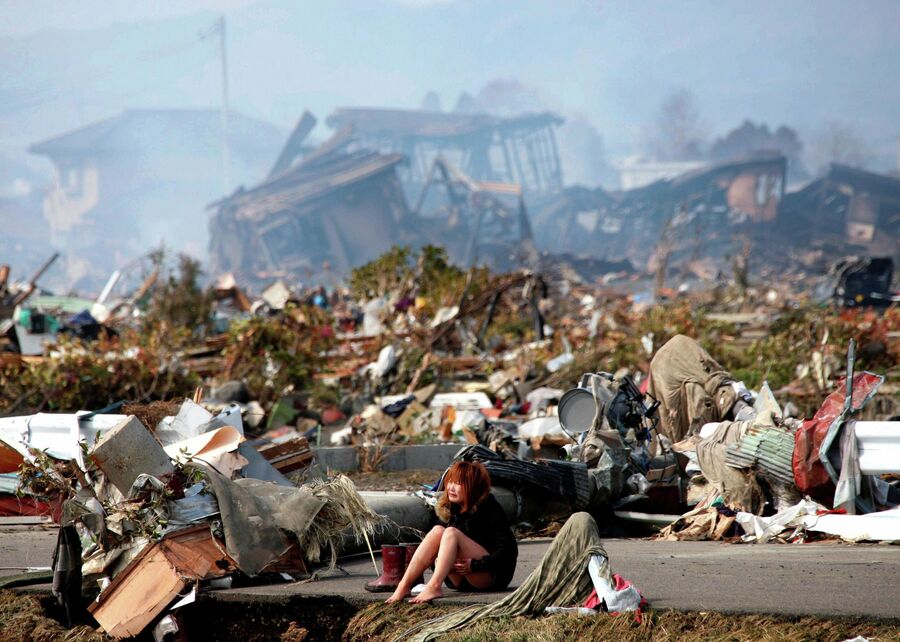 Женщина сидит на дороге в разрушенном городе Натори, префектура Мияги, после мощного землетрясения и цунами на севере Японии. 13 марта 2011 года