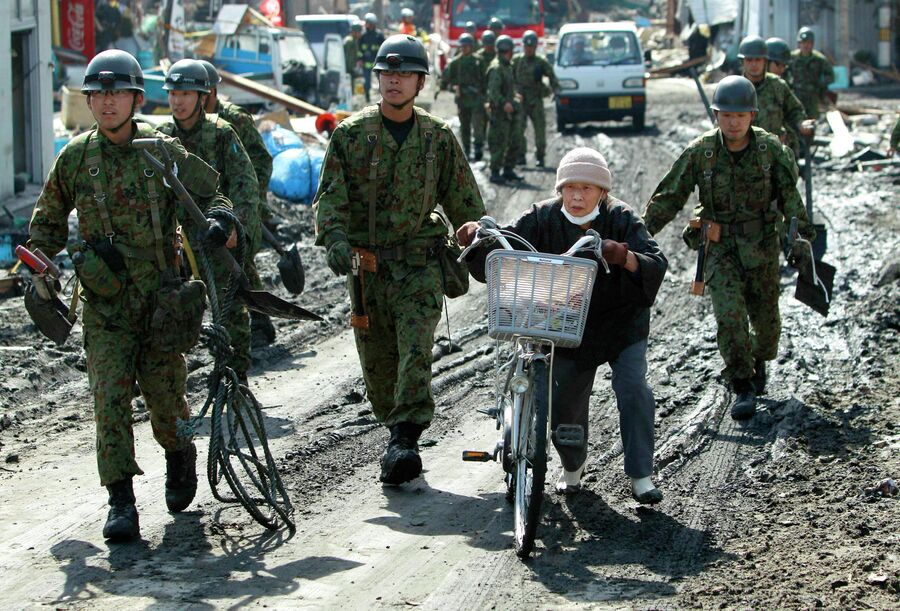 Солдаты Сухопутных сил самообороны Японии призывают пожилую женщину перебраться на возвышенность во время предупреждения о цунами в гавани города Сома, префектура Фукусима, Япония. 14 марта 2011 года
