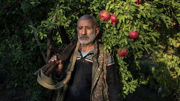 Местный житель Анушаван стоит в гранатовом саду во дворе своего дома. В его руке старый автомат Калашникова, который остался у него с первой карабахской войны. Село Ухтасар