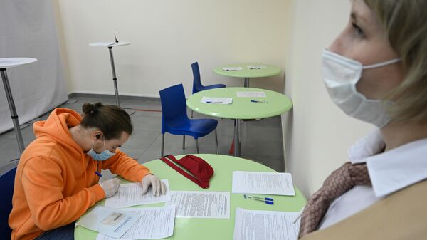 Молодой человек заполняет анкету перед вакцинацией в мобильном пункте вакцинации от COVID-19  в торговом центре Тройка в Москве