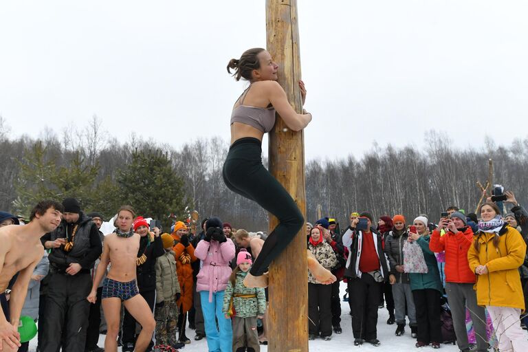 Участница народных гуляний лезет по столбу во время празднования Бакшевской Масленицы в Московской области