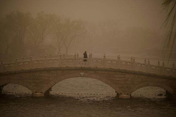 Женщина переходит мост через озеро Хоухай во время песчаной бури в Пекине