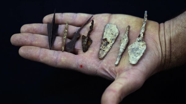 Сотрудник держит древние наконечники стрел и копий, недавно обнаруженных в пещерах Иудейской пустыни