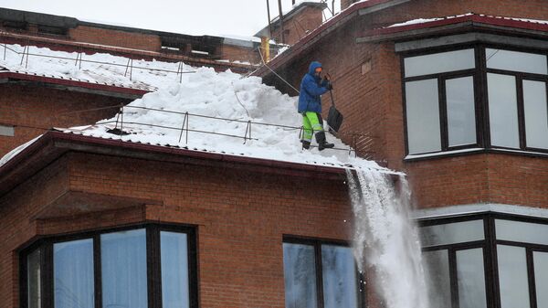 Рабочий очищает крышу дома от снега
