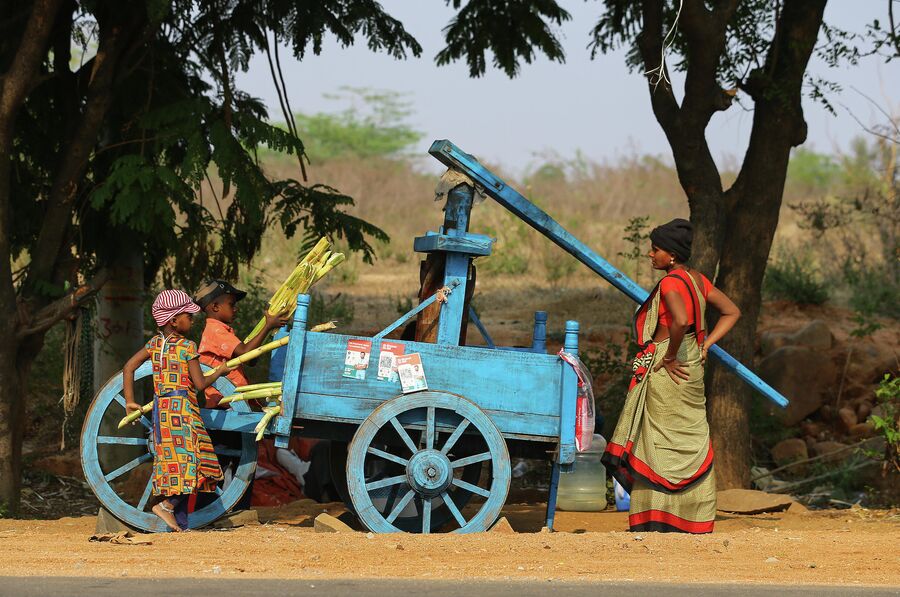Индийские дети помогают женщине извлекать сок из сахарного тростника на окраине Хайдарабада, Индия