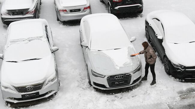 Девушка чистит автомобиль от снега на стоянке 