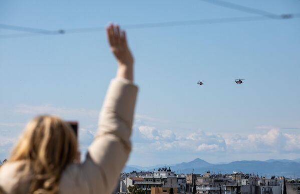 Жительница Афин приветствует вертолеты ВВС Греции, участвующие на параде, посвященном 200-летию независимости Греции