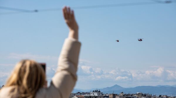 Жительница Афин приветствует вертолеты ВВС Греции, участвующие на параде, посвященном 200-летию независимости Греции