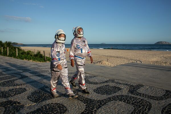 Люди в костюмах космонавтов гуляют по пляжу Ипанема в Рио-де-Жанейро