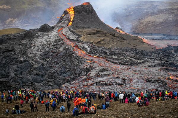 Туристы смотрят на лаву, текущую из извергающегося вулкана Фаградальсфьяль в Исландии