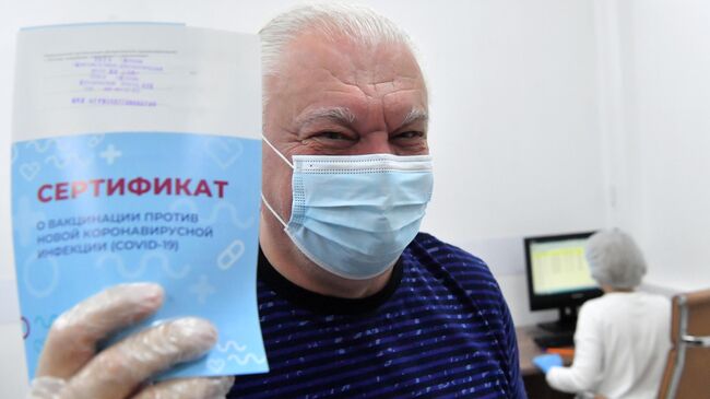 Пожилой мужчина демонстрирует сертификат о вакцинации против новой короновирусной инфекции (COVID-19), полученный после прививки в центре госуслуг Мои документы