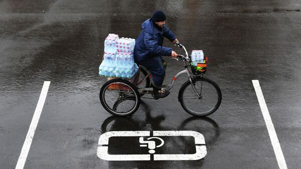 Мужчина на велосипеде везет упаковки с бутилированной водой по улице Москвы