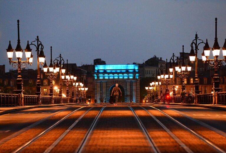 Мужчина идет по мосту Pont de Pierre, подсвеченному синим цветом в рамках международной акции Зажги синим (Light It Up Blue) в Бордо, Франция