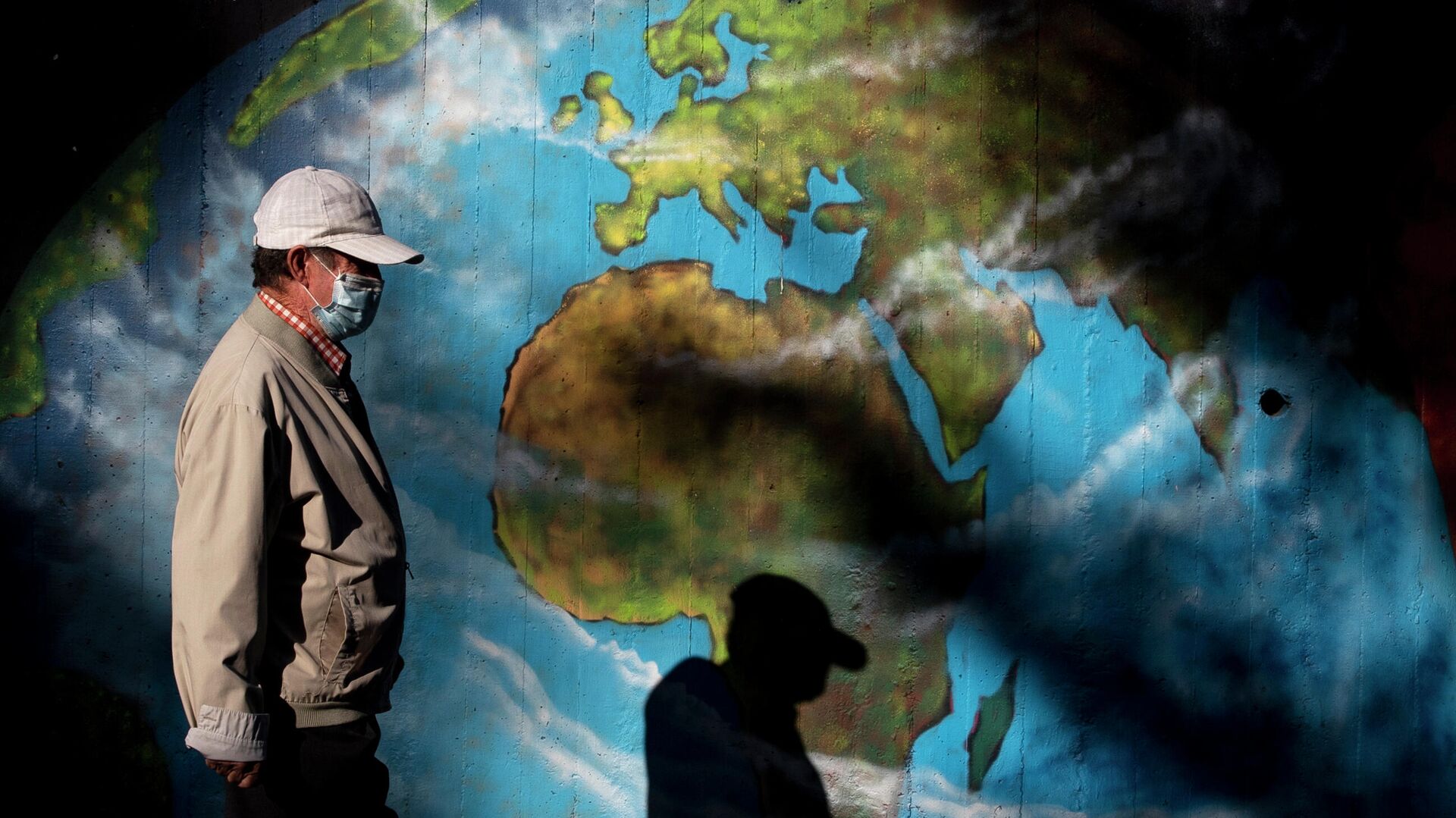 Мужчина в защитной маске проходит мимо граффити с изображением глобуса во время пандемии коронавируса в мире  - РИА Новости, 1920, 30.06.2021