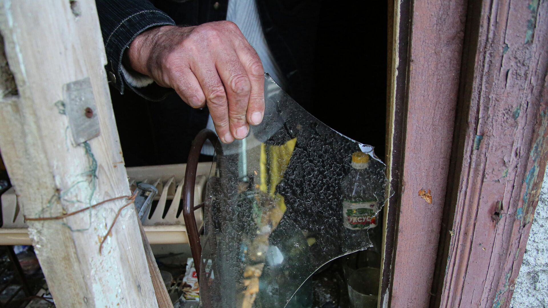 Местный житель из села Васильевка Донецкой области держит кусок разбитого стекла из разбитого окна жилого дома, пострадавшего в результате обстрела - РИА Новости, 1920, 10.04.2021