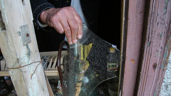 Местный житель из села Васильевка Донецкой области держит кусок разбитого стекла из разбитого окна жилого дома, пострадавшего в результате обстрела