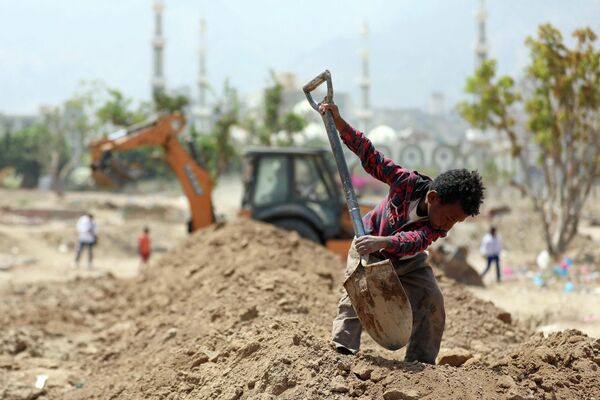 Йеменский рабочий помогает экскаватору рыть могилы для жертв COVID-19 на кладбище в городе Таиз
