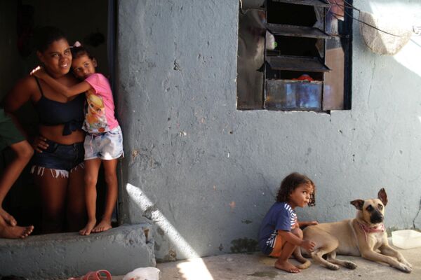 Моник Фернанда де Асис у дверей своего дома с дочерью Эстер и сыном Мигелем, играющим с собакой