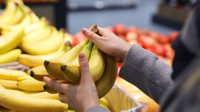 Покупательница выбирает бананы в магазине