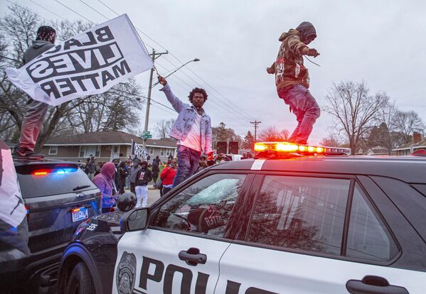 Участники акции протеста на капоте полицейского автомобиля в центре города Бруклин-Сентер в штате Миннесота, США