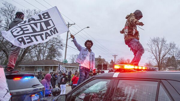 Участники акции протеста на капоте полицейского автомобиля в центре города Бруклин-Сентер в штате Миннесота, США