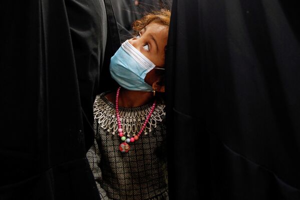 Девочка в маске на лице стоит в очереди вместе с матерью в Наджафе, Ирак. 12 апреля 2021 года