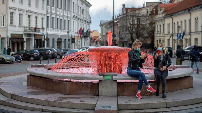 Девушки в защитный масках фотографируются у фонтана, окрашенного в красный цвет, во всемирный день гемофилии в Вильнюсе