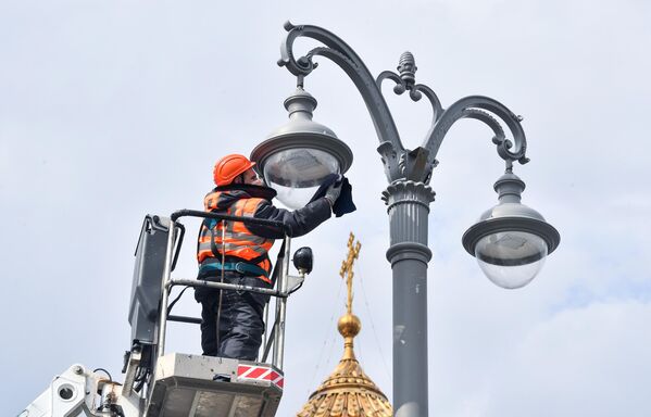 Сотрудник коммунальной службы протирает плафон фонаря наружного освещения на Пречистенской набережной в Москве